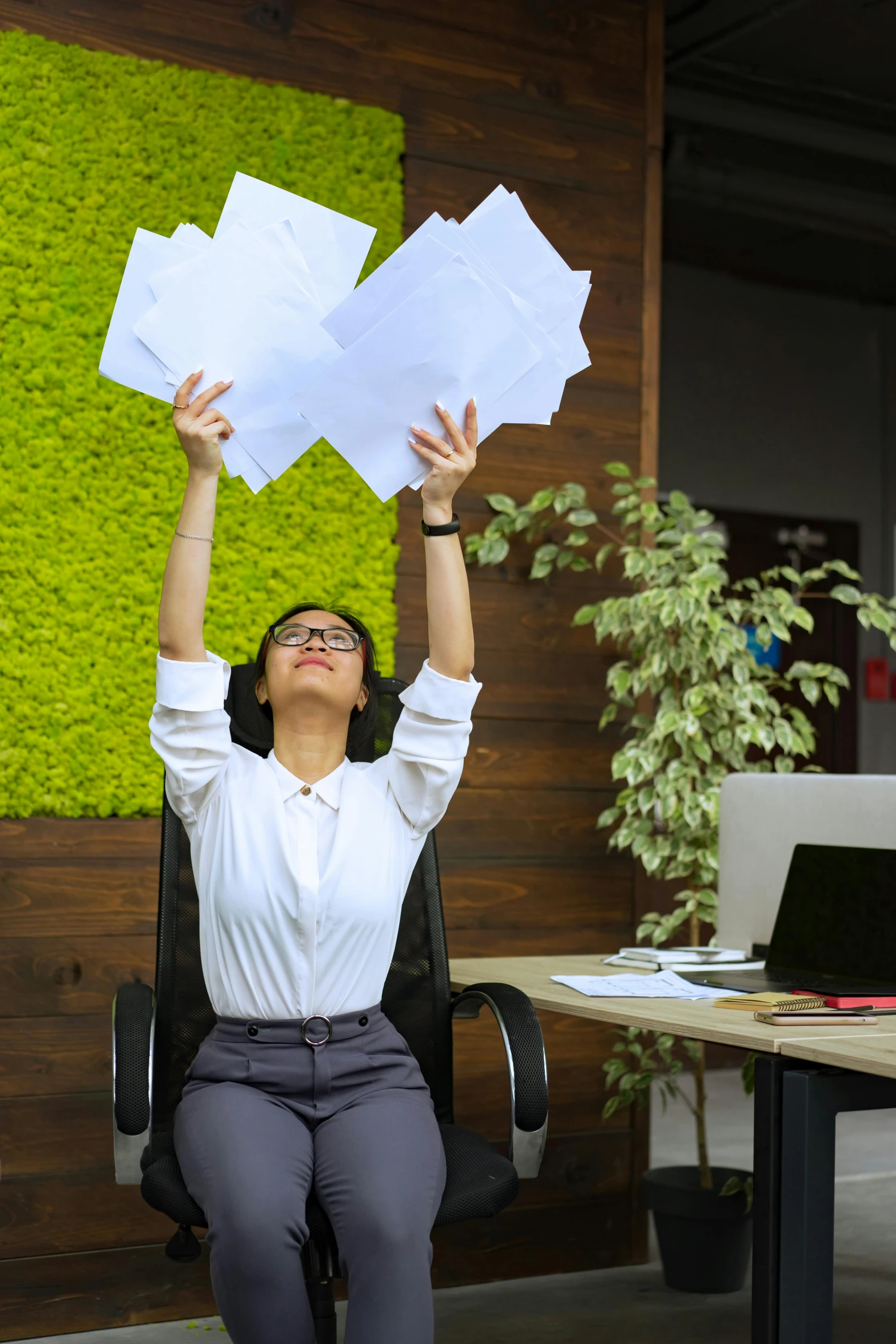 a woman sitting in a chair holding papers above her head, pexels contest winner, office ceiling panels, arms stretched out, sustainable materials, overflowing energy