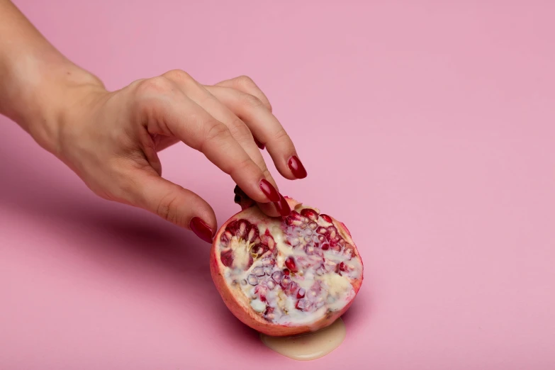 a woman's hand holding a pomegranate on a pink background, by Will Ellis, trending on pexels, arabesque, made of food, porcelain skin ”, cut-away, wolfy nail