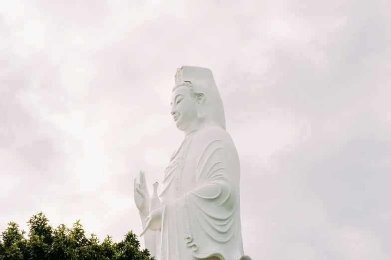 a large white statue sitting on top of a lush green field, a statue, unsplash, guanyin, portrait image, white sky, half image