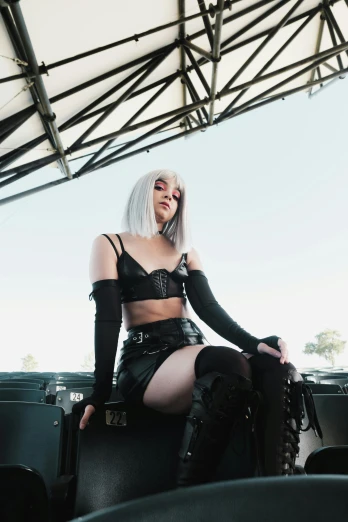 a woman sitting on a chair in a stadium, an album cover, inspired by Glòria Muñoz, cosplay on black harley queen, platinum hair, loish |, 2019 trending photo