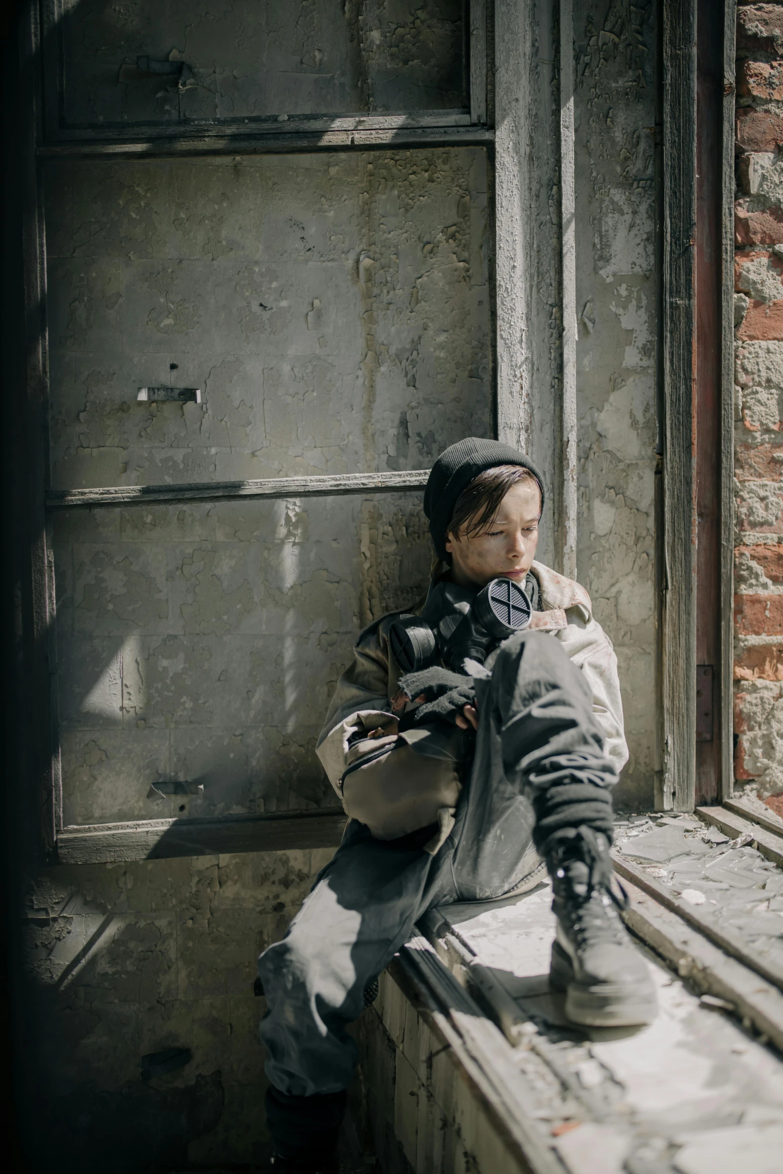 a little boy that is sitting on a window sill, inspired by ashley wood, pexels contest winner, visual art, wearing tactical gear, grungy woman, norilsk, broken down grey wall