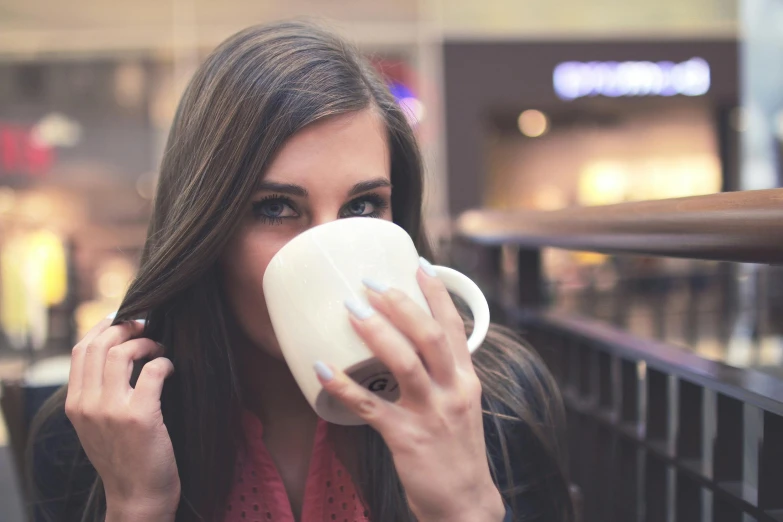 a woman sitting at a table drinking a cup of coffee, pexels contest winner, happening, girl with dark brown hair, at a mall, manuka, porcelain skin ”