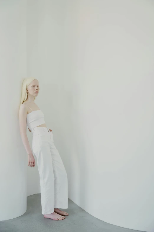 a woman leaning against a wall in a white room, inspired by Vanessa Beecroft, unsplash, intense albino, white pants, portrait of white teenage girl, color photo