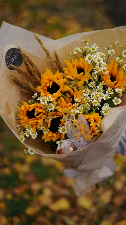 a person holding a bunch of flowers in their hand, shades of gold display naturally, sunflowers in the background, autumnal colours, thumbnail