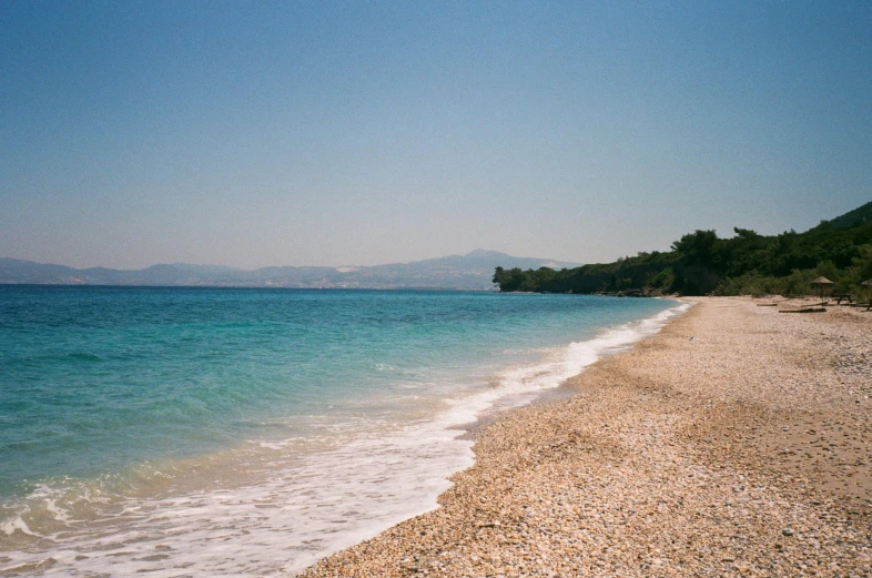 a sandy beach next to the ocean on a sunny day, inspired by Constantine Andreou, unsplash, 1990's photo, medium format, greece, pale head