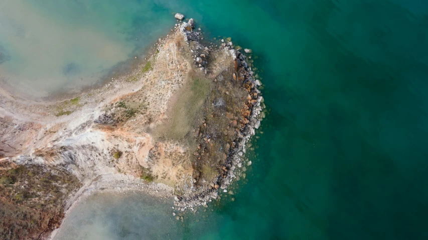 an aerial view of an island in the middle of the ocean, by Peter Churcher, unsplash contest winner, hurufiyya, rocky lake shore, burned, structural geology, slightly blurred