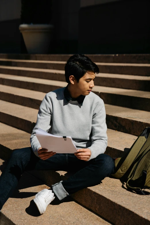 a man sitting on steps reading a piece of paper, pexels contest winner, academic art, non binary model, asian male, college students, holding a clipboard