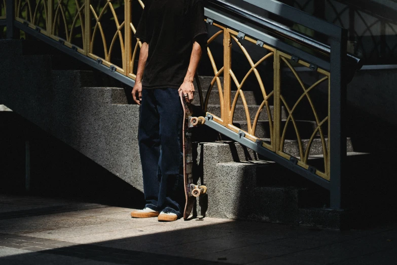 a man standing next to a set of stairs holding a skateboard, unsplash, “ iron bark, low detailed, editorial image, instagram picture