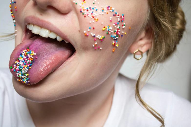 a woman sticking her tongue out with sprinkles on her face, an album cover, inspired by Bert Stern, trending on pexels, closeup - view, underbite, sci - fi jewellery, amanda lilleston