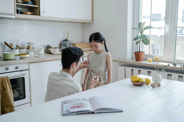 a man standing next to a woman in a kitchen, by Emma Andijewska, pexels contest winner, young asian girl, lawther sit at table playing dnd, tiny girl looking on, comforting