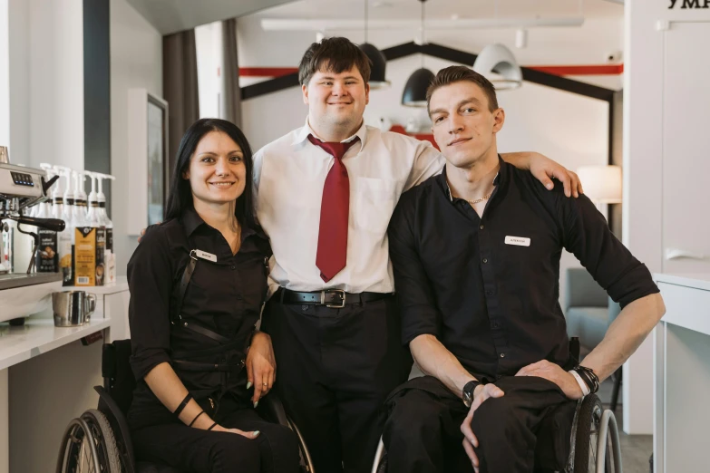 a man sitting in a wheel chair next to two women, a portrait, by Emma Andijewska, unsplash, wearing rr diner uniform, confident pose, edmund blair and charlie bowater, server in the middle