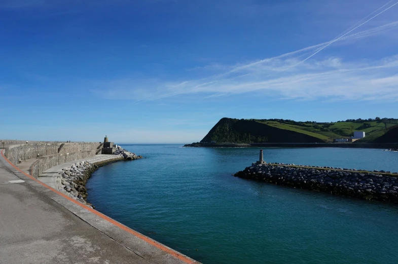 a man riding a bike down a road next to a body of water, a picture, inspired by John Marin, pexels contest winner, dover castle, near a jetty, cyan and green, panorama