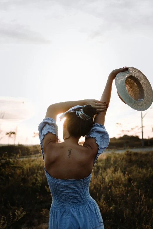 a woman in a blue dress holding a hat, by Niko Henrichon, pexels contest winner, happening, sun down, showing her shoulder from back, country style, various posed