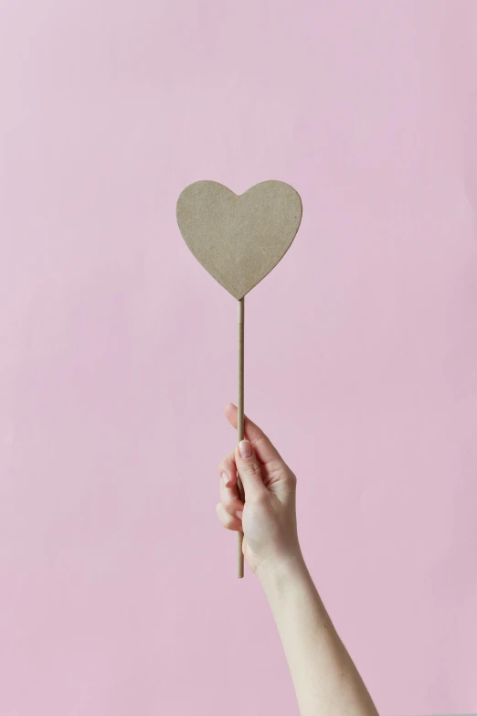 a person holding a paper heart on a stick, taupe, detailed product shot, brass plated, single subject