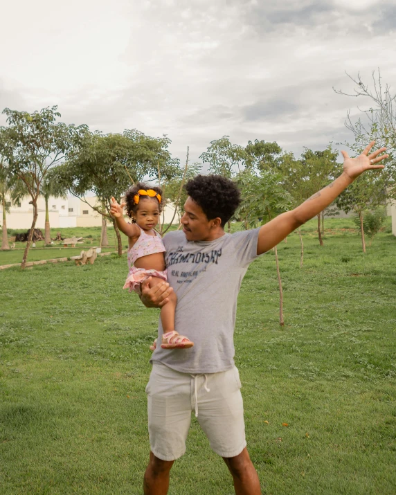 a man holding a little girl on top of a lush green field, pexels contest winner, renaissance, with afro, in chuquicamata, with fruit trees, in the yard