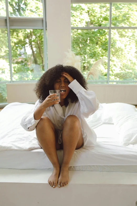 a woman sitting on top of a bed next to a window, drinking cough syrup, sza, wearing white pajamas, cervix awakening