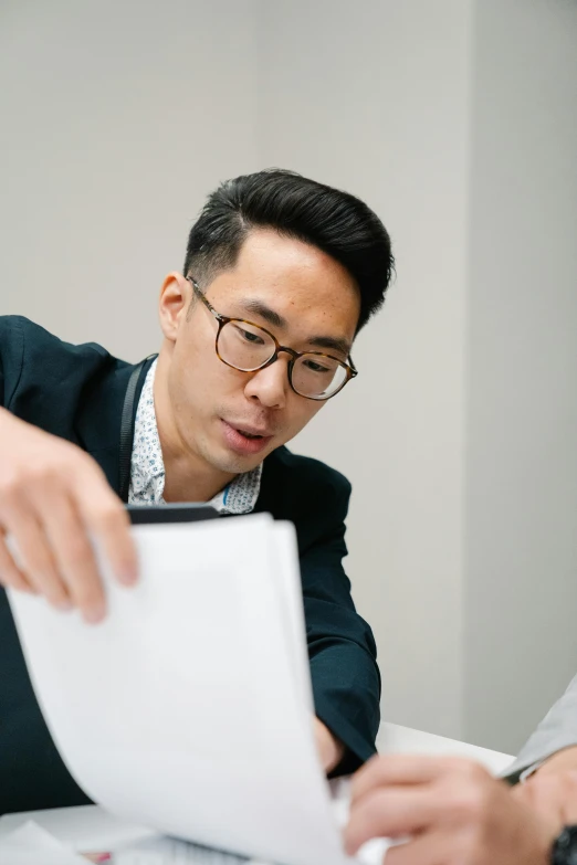 a couple of men sitting at a table with papers, inspired by Fei Danxu, pexels contest winner, holding a clipboard, wearing black frame glasses, professional profile picture, janice sung