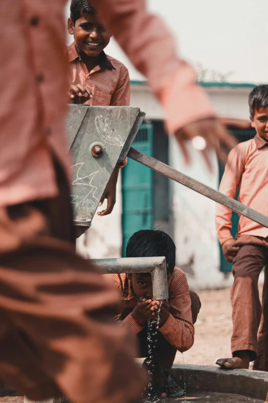 a group of children standing around a water pump, pexels contest winner, auto-destructive art, swinging a big sword, india, school courtyard, toy guillotine