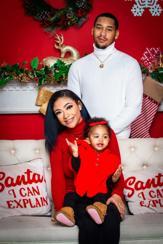 a man and woman sitting on a couch in front of a christmas tree, a photo, instagram, portrait of vanessa morgan, husband wife and son, solid color backdrop, promo image