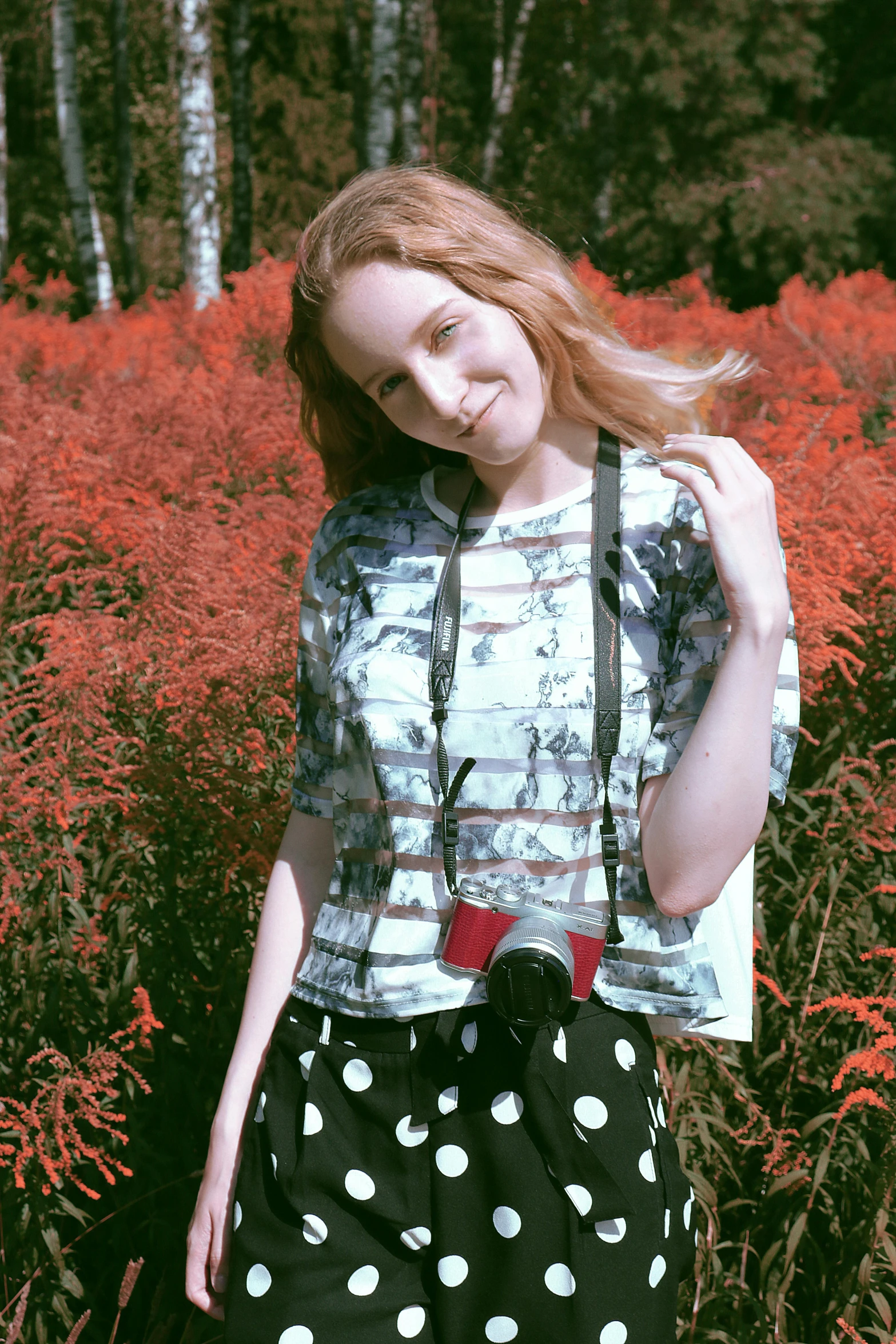 a woman standing in a field of tall grass, a colorized photo, unsplash, happening, julia garner, patterned clothing, holding a camera, with red hair