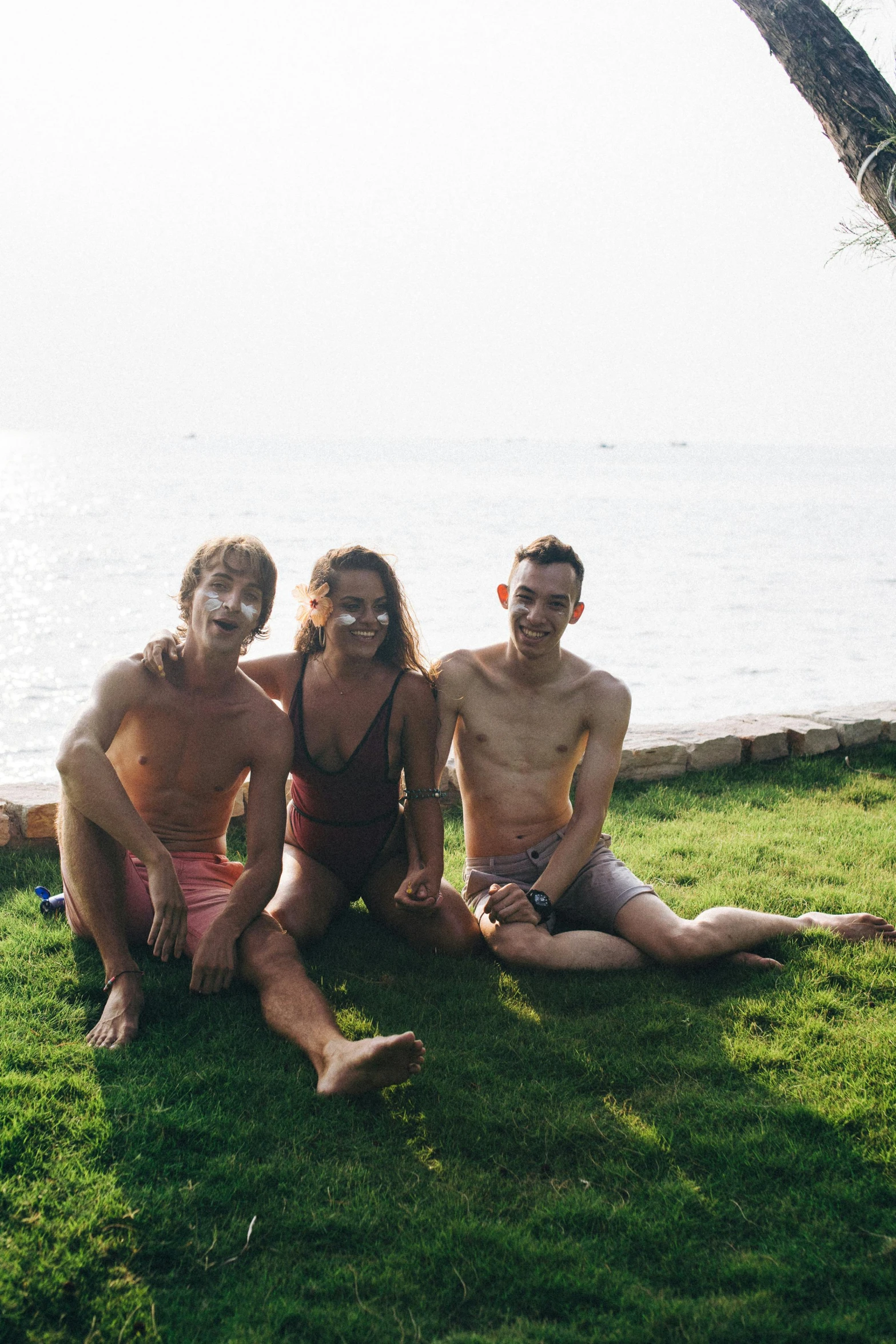 a group of people sitting on top of a lush green field, posing on the beach, the three moiras, slightly muscular, roomies