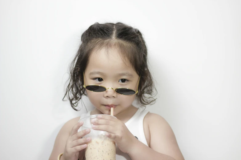 a little girl holding a drink in front of her face, inspired by Nara Yoshitomo, pexels contest winner, photorealism, wearing gold glasses, drink milkshakes together, young cute wan asian face, **cinematic