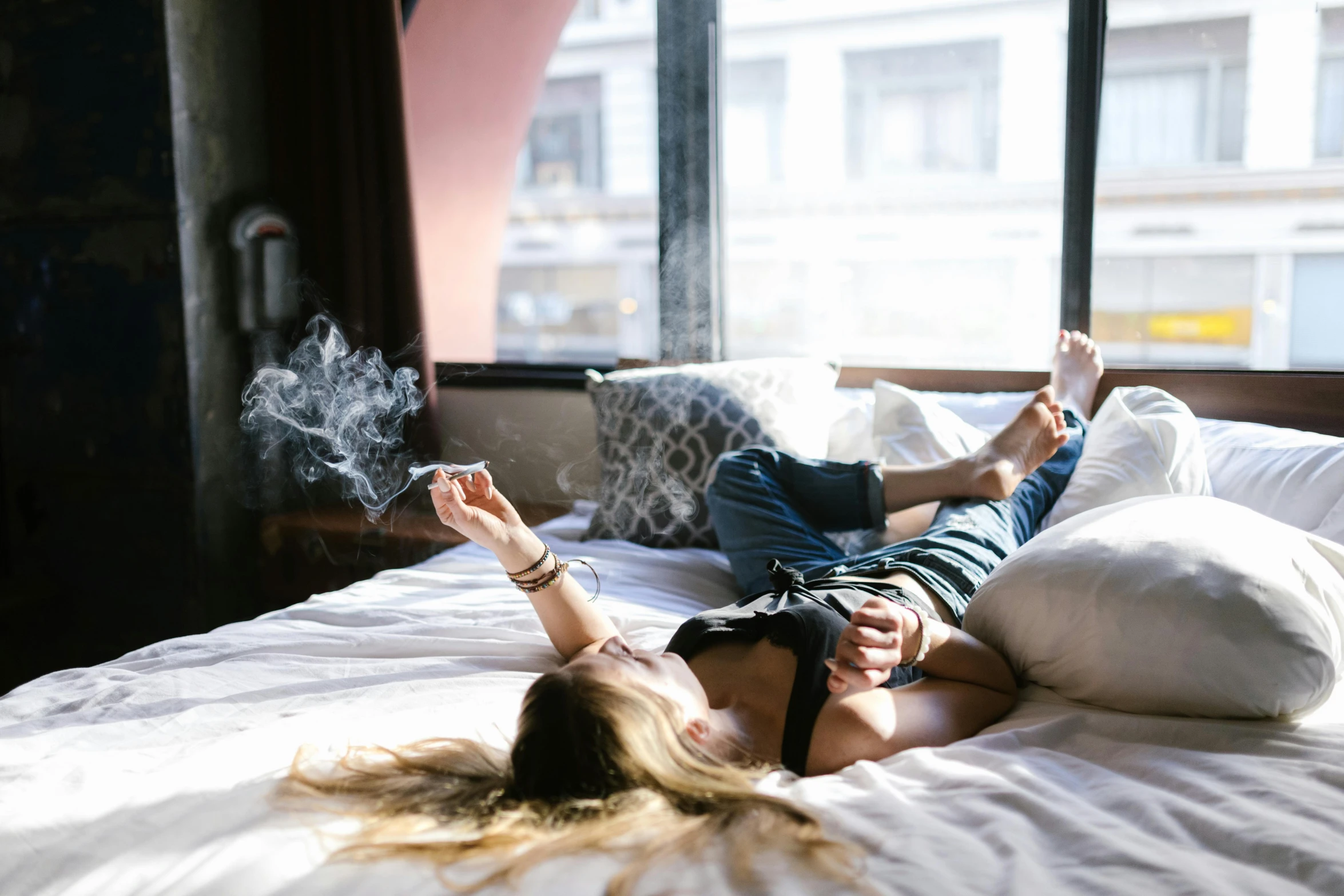 a woman laying on top of a bed next to a window, trending on unsplash, harry potter smoking weed, hotel room, smoke grenades, sydney hanson