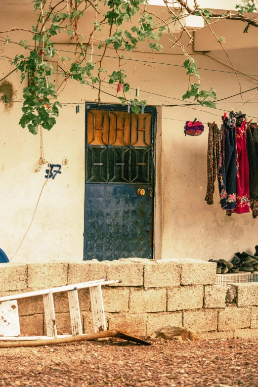 a man sitting on a bench in front of a house, by Elsa Bleda, trending on unsplash, rojava, laundry hanging, in a village, doorway