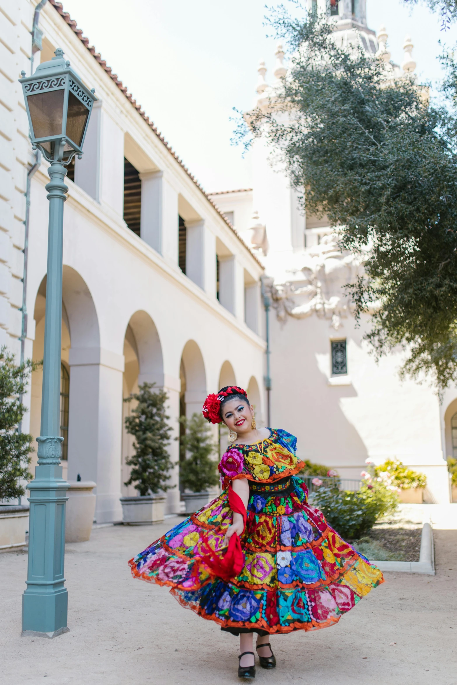 a woman in a colorful dress standing in front of a building, inspired by Frida Kahlo, renaissance, clown waving hello, the city of santa barbara, university, minnie mouse