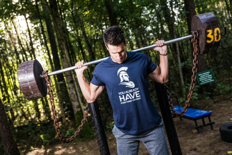 a man lifting a barbell in the woods, a portrait, inspired by Hercules Seghers, unsplash, private press, batman t shirt, navy shirt, hidden message, donkey riding a playground swing