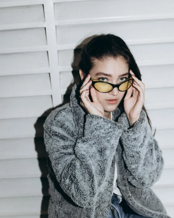 a woman wearing glasses sitting on top of a bed, inspired by Elsa Bleda, trending on pexels, yellow fur, bella poarch, grey clothes, good lighted photo