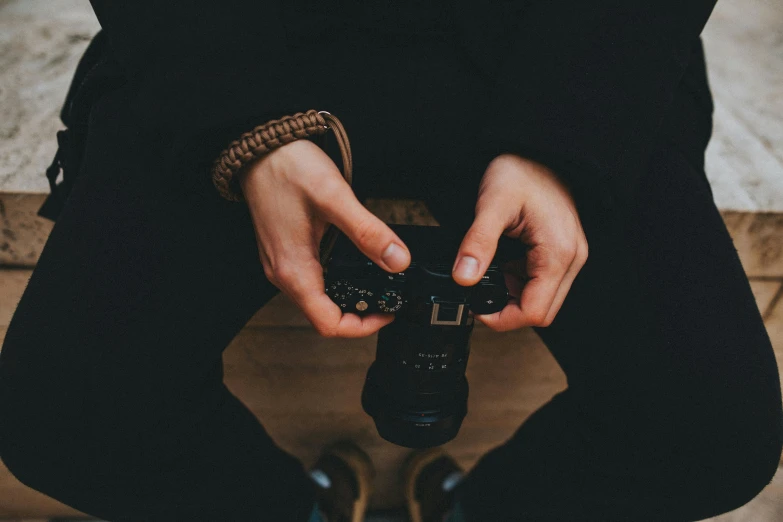 a close up of a person holding a camera, pexels contest winner, sitting with wrists together, top - down photograph, wearing leather, dark photo
