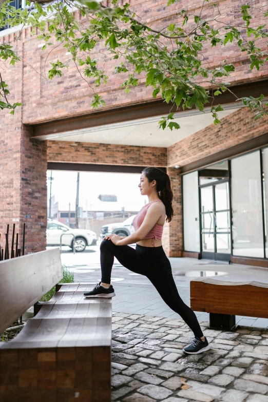 a woman sitting on a bench in front of a building, dynamic stretching, lush brooklyn urban landscaping, knee, louise zhang