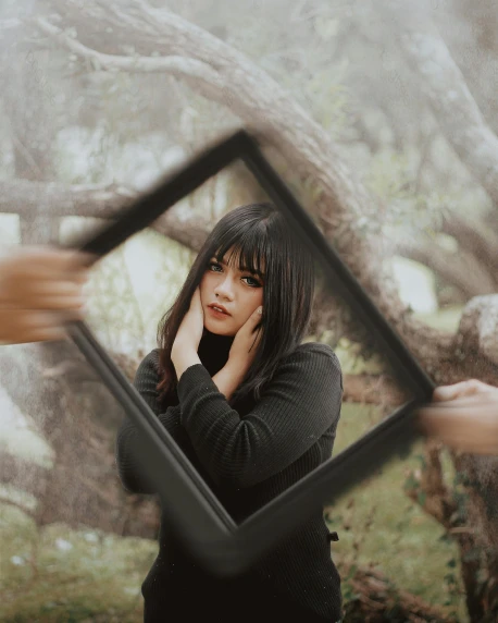 a woman holding a picture frame in front of her face, inspired by Elsa Bleda, pexels contest winner, surrealism, she has black hair with bangs, in a tree, square pictureframes, asian women