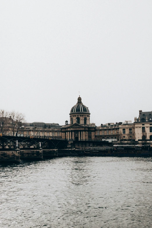 a bridge over a body of water with a building in the background, by Raphaël Collin, trending on unsplash, paris school, overcast gray skies, neoclassical tower with dome, private school, exterior view