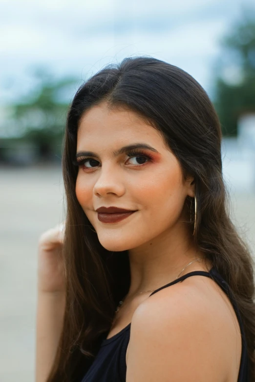 a woman in a black dress posing for a picture, inspired by Emma Ríos, trending on pexels, beauty mark on cheek, brown dark hair, square, multicolored