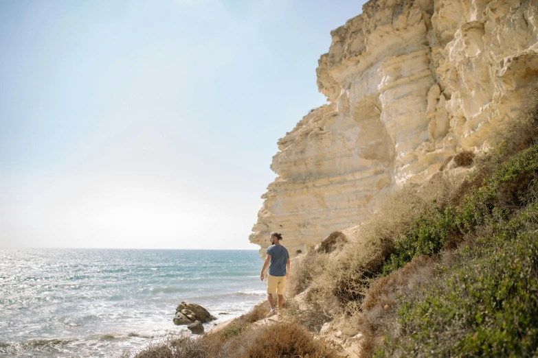 a man standing on top of a cliff next to the ocean, les nabis, secret valley, profile image, limestone, chalk cliffs above