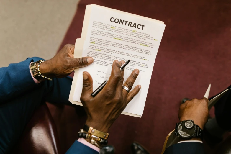 a man sitting in a chair holding a pen and paper, by Julia Pishtar, pexels contest winner, making a deal with the devil, black man with afro hair, back of hand on the table, patent registry