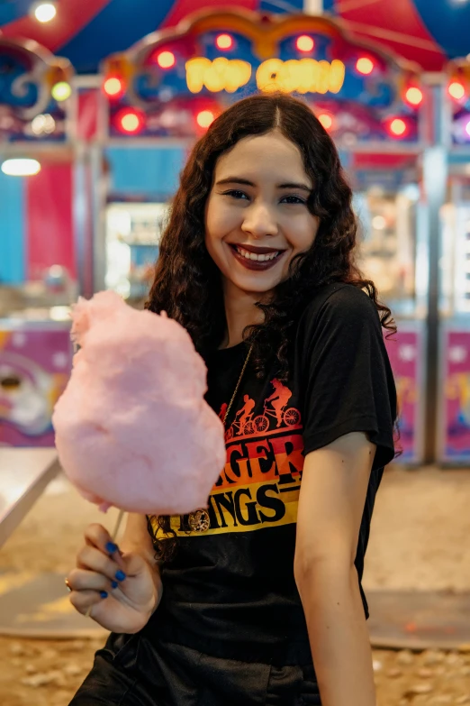 a woman sitting on a bench holding a cotton candy floss, pexels contest winner, happening, wearing a black tshirt, chuck e. cheese, background image, smiling young woman