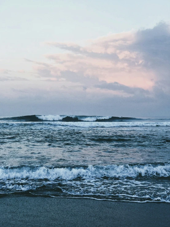 a man standing on top of a beach next to the ocean, by Carey Morris, pexels contest winner, rippling oceanic waves, overcast dusk, hyperdetailed photo, two medium sized islands