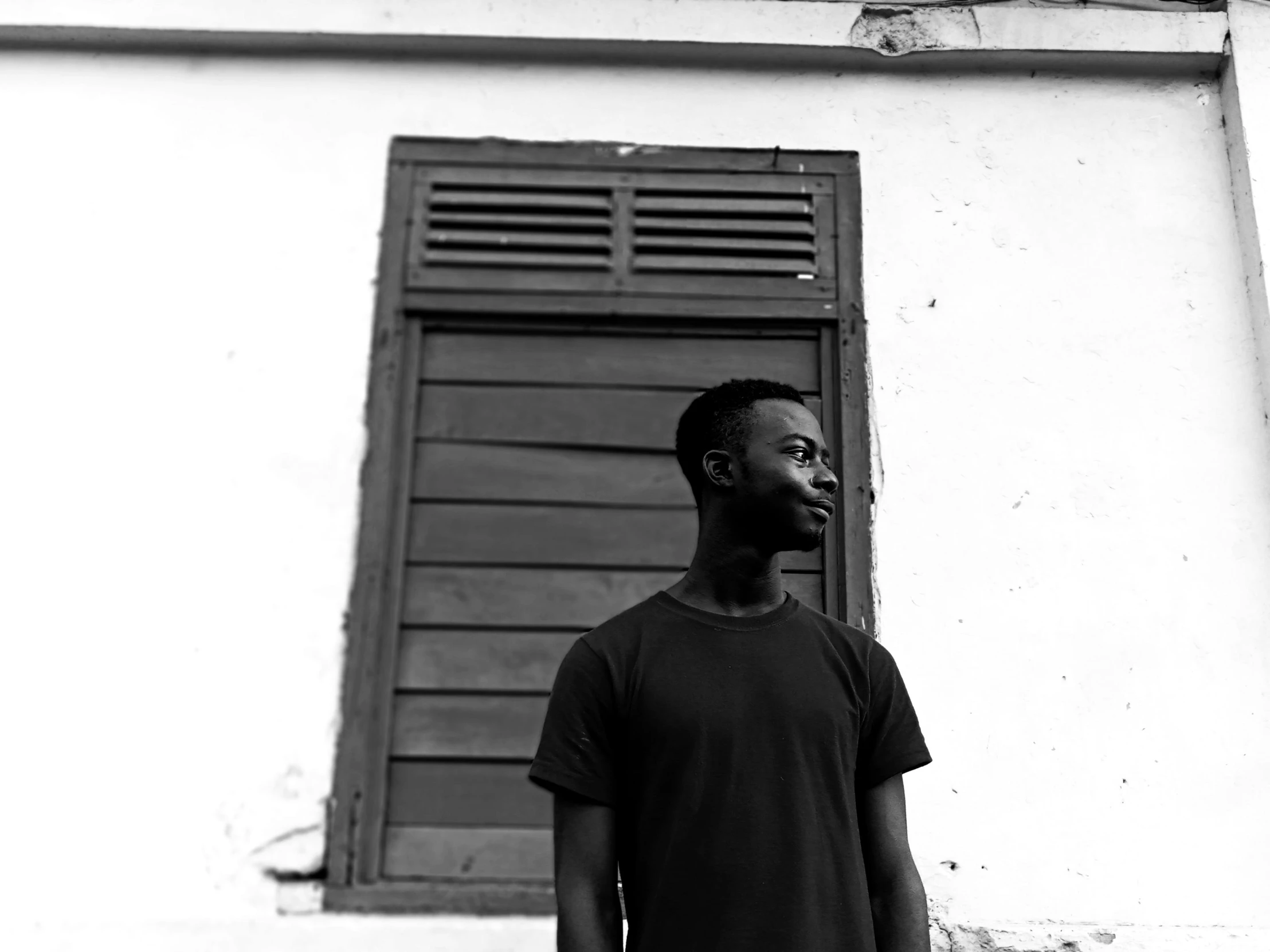 a black and white photo of a man standing in front of a building, by Dean Ellis, pexels contest winner, brown skinned, around 1 9 years old, sussy baka, slightly minimal