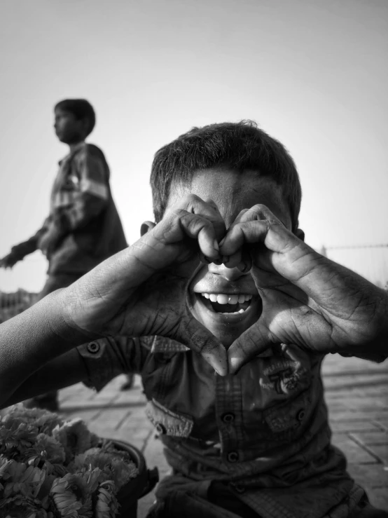 a black and white photo of a boy covering his eyes, by Ibrahim Kodra, expressing joy. by krenz cushart, smiley, full heart - shaped face, kids playing