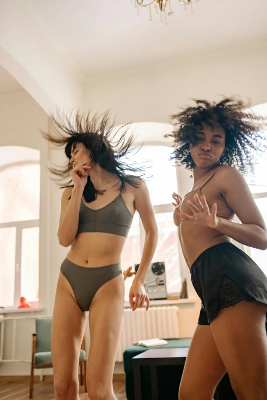 a couple of women standing on top of a wooden floor, by Matija Jama, trending on pexels, happening, wavy lingeries, she is dancing, messy black hair, infp young woman