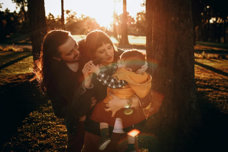 a woman holding a baby while standing next to a tree, pexels contest winner, golden sunlight, portrait of family of three, avatar image, straya