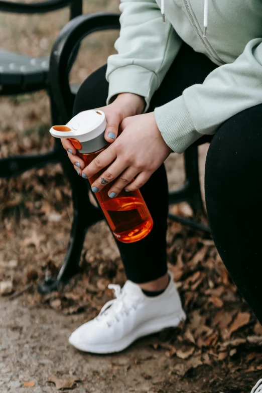 a woman sitting on a bench holding a cup of coffee, maple syrup fluid, wearing fitness gear, orange and white, zoomed out