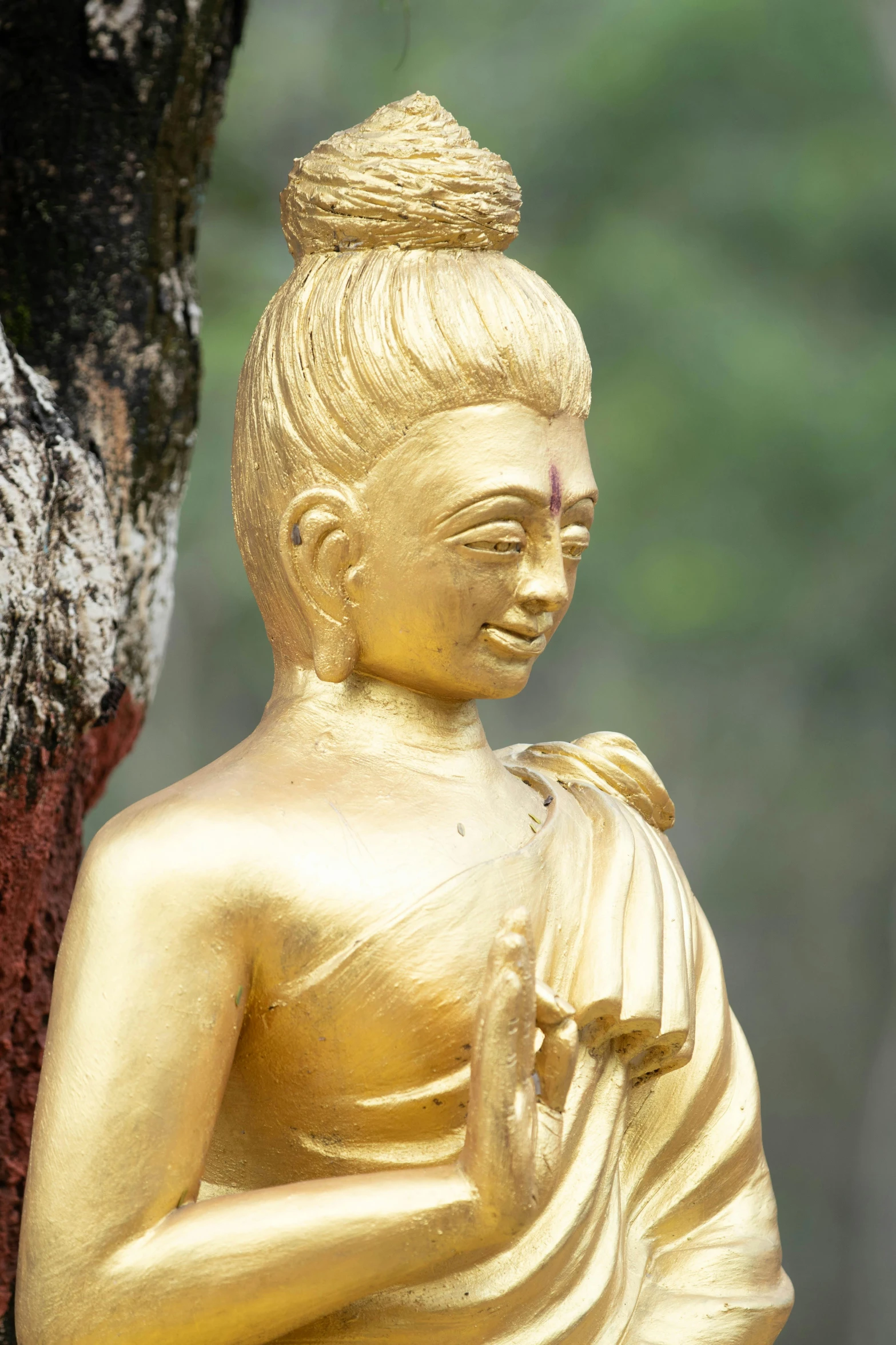 a golden buddha statue sitting next to a tree, white haired deity, aged 2 5, gold plated, over the shoulder