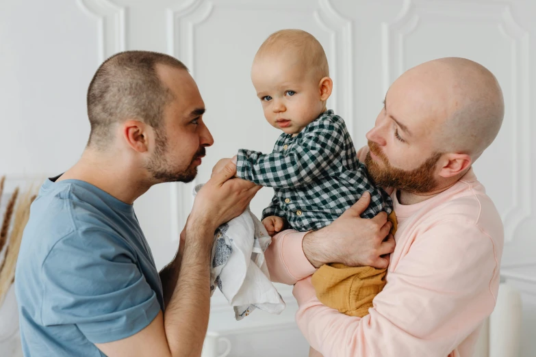 a man holding a baby in his arms, by Adam Marczyński, pexels contest winner, two male, bowater charlie and brom gerald, holding an epée, avatar image