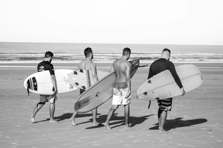 a group of men standing on top of a beach holding surfboards, a black and white photo, by Kristian Zahrtmann, pexels contest winner, walking away from the camera, profile image, six sided, maintenance