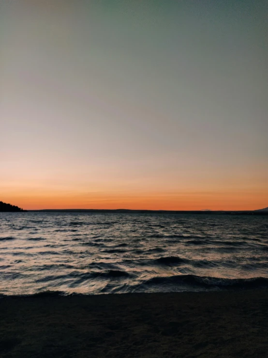 a man standing on top of a beach next to the ocean, a picture, unsplash, romanticism, orange lit sky, detailed lake in background, 2 5 6 x 2 5 6 pixels, reddit post