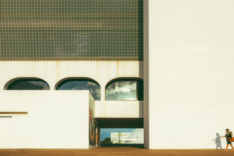 a couple of people walking in front of a building, inspired by Ned M. Seidler, unsplash, brutalism, cinestill 800t 50mm eastmancolor, archs, 1990 photograph, white building